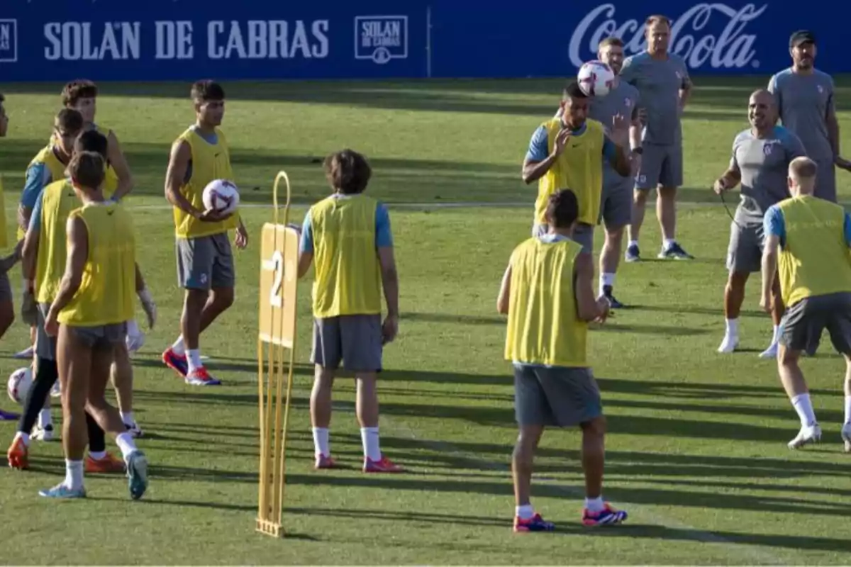 Football players training on a football pitch in yellow bibs with coaches watching.