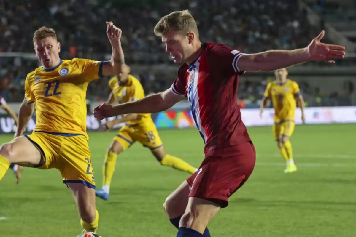 Football players in action during a match, one in yellow uniform and one in red uniform.