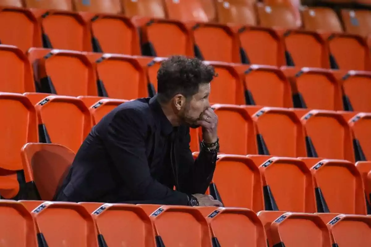 Thoughtful man sitting alone in the stands of an empty stadium with orange seats.