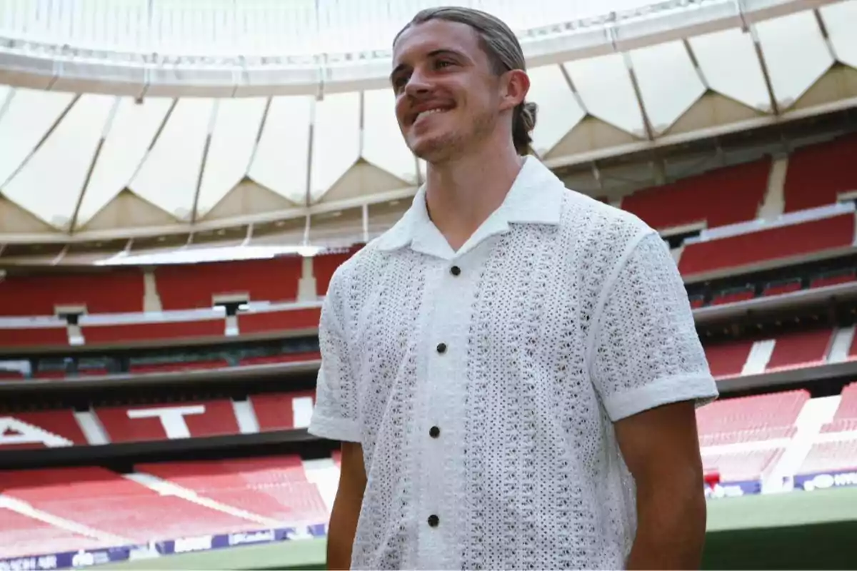 A man in a white lace shirt stands in an empty football stadium.