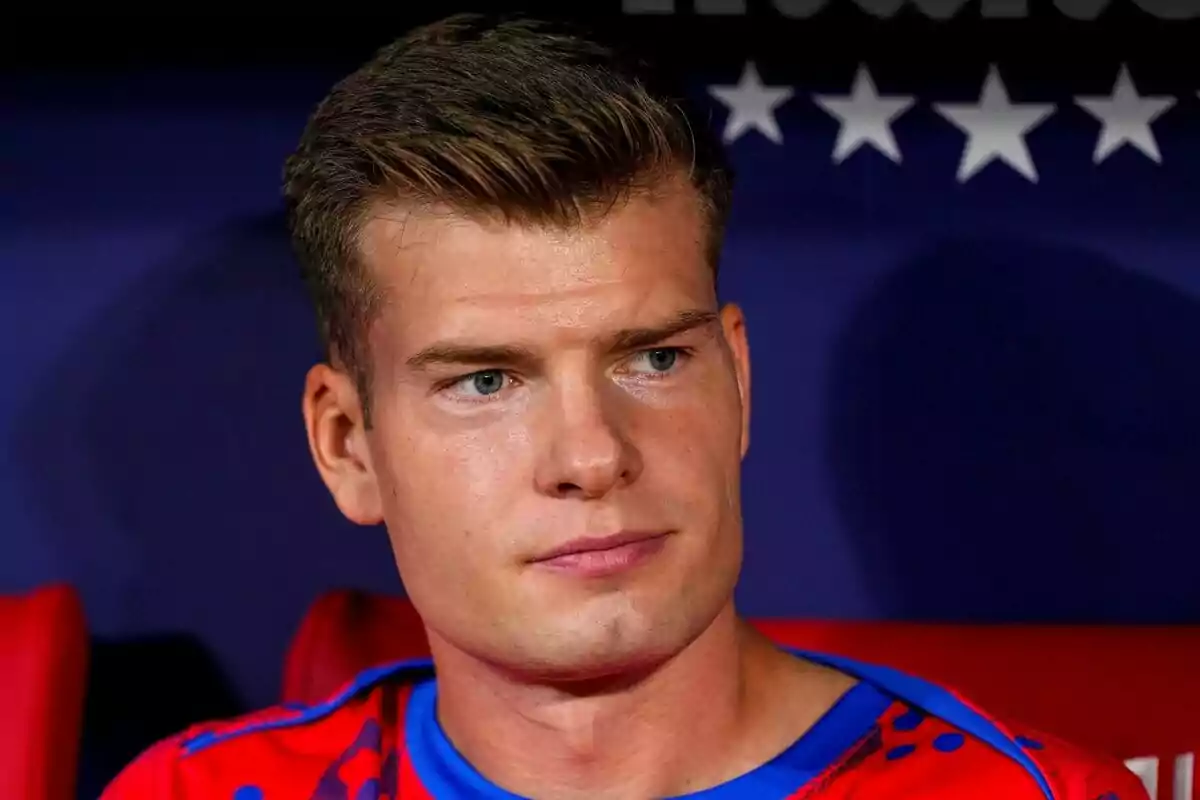 A man in a red and blue t-shirt looking to the side with a serious expression.