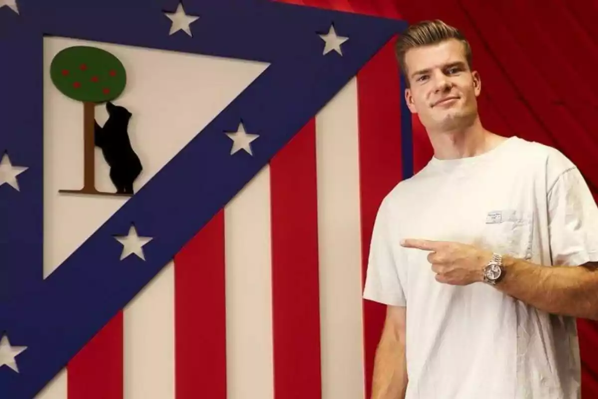 A man in a white T-shirt points to the Atlético de Madrid crest.