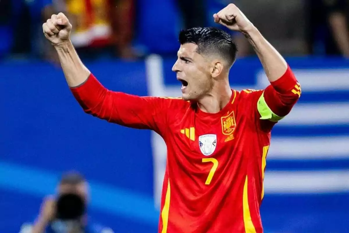 Soccer player in red uniform celebrating with arms raised.