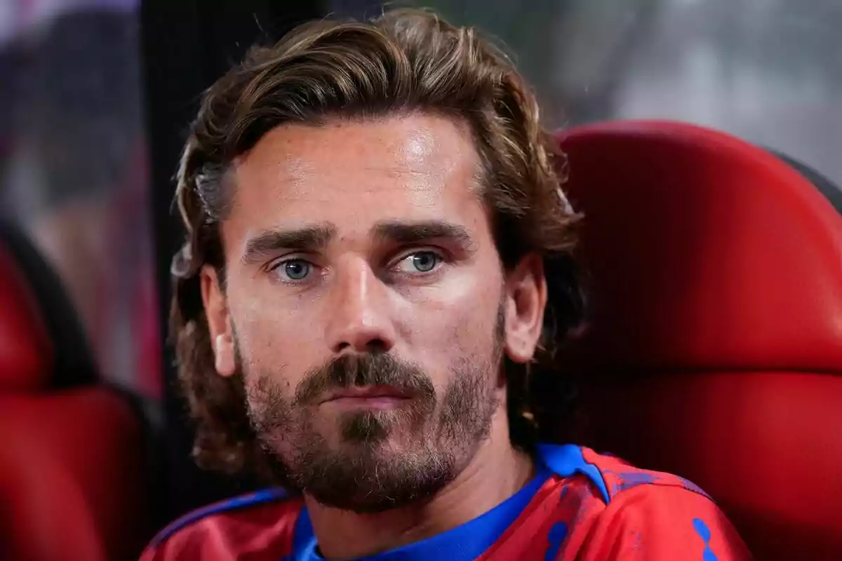 Man with beard and long hair sitting on a red seat.