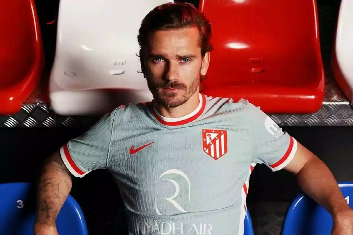 A football player wearing an Atlético Madrid shirt sits in a stand with red, white and blue seats.