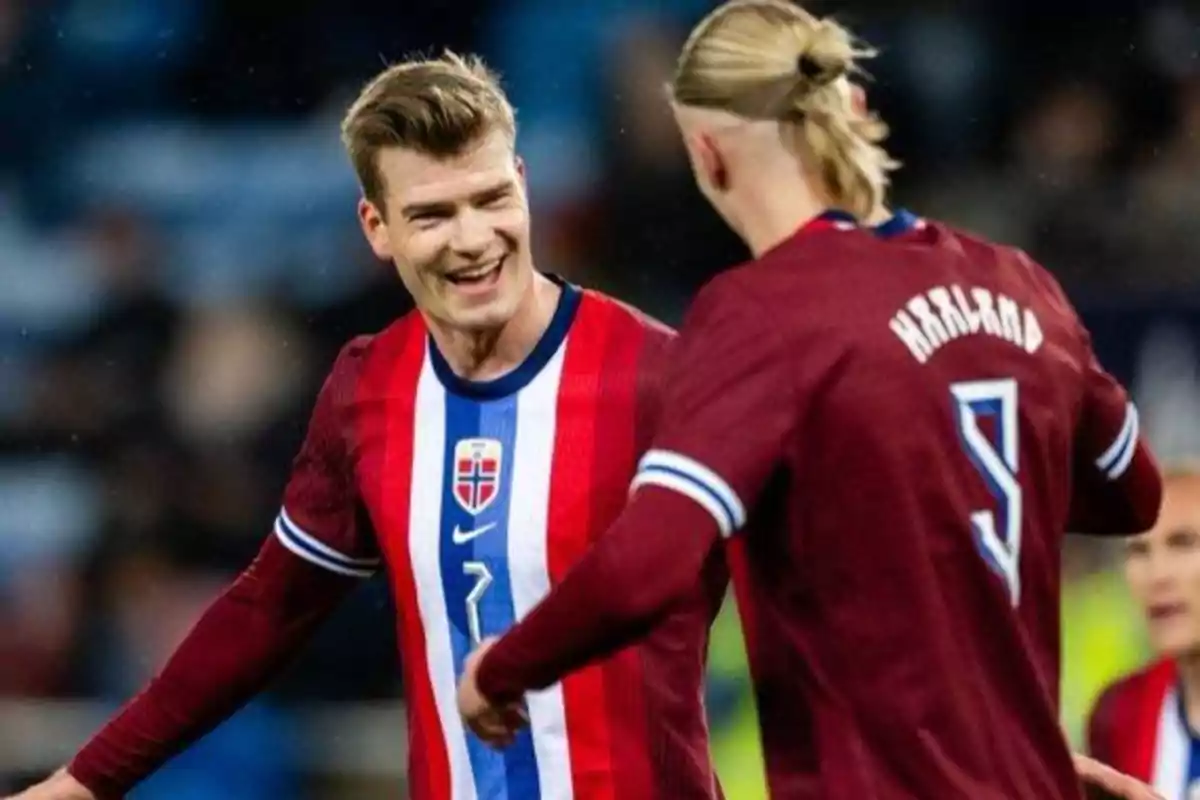 Two soccer players in red and blue uniforms celebrate on the field.