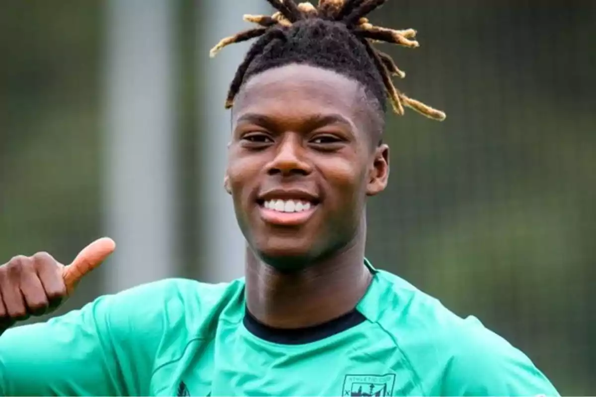 A smiling young footballer in a green jersey with his thumb up.