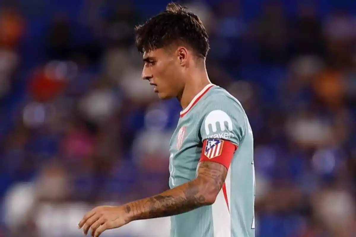 Soccer player in green uniform and captain's armband in a stadium.