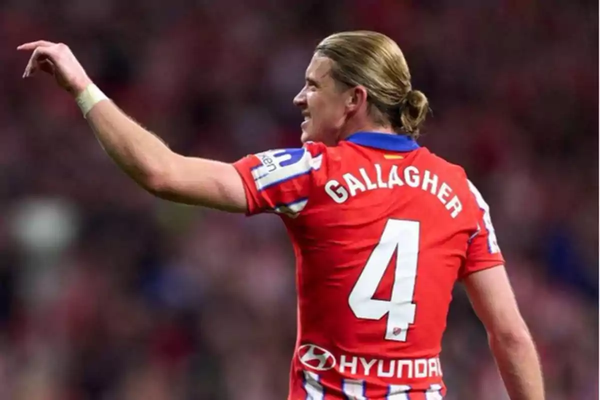 Football player wearing a red and white number 4 jersey with the name Gallagher on the back, pointing with his arm.