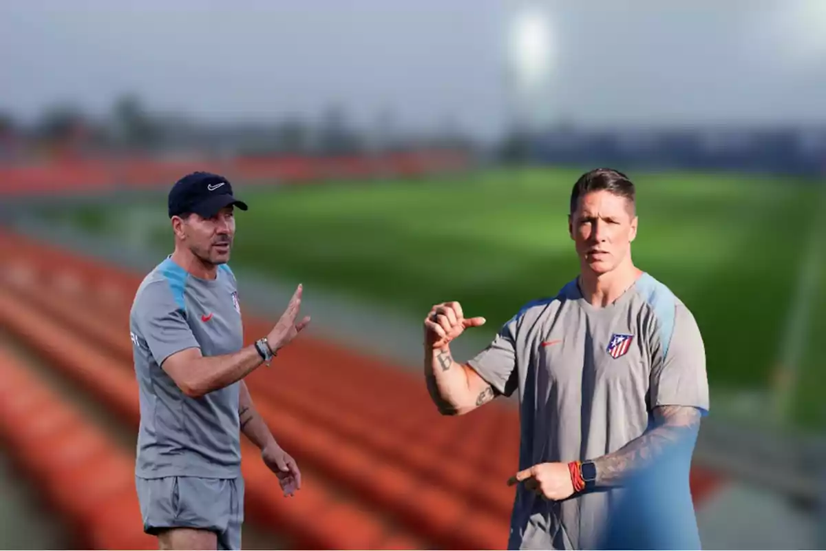 Two men wearing Atlético de Madrid sportswear are on a training pitch, one of them is wearing a cap and the other has tattoos on his arm.