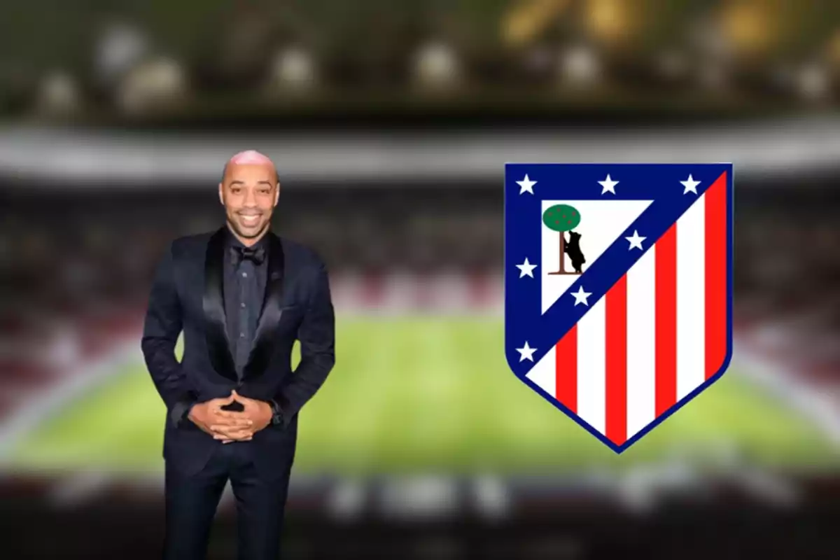 A man in a dark suit smiles in front of a football stadium, next to the Atlético de Madrid crest.