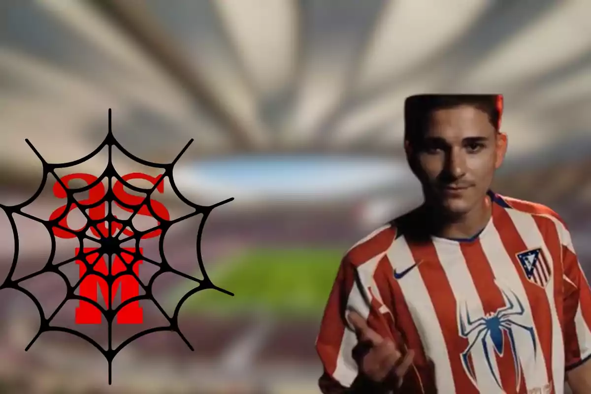 A man wearing an Atletico Madrid football shirt with a spider design on the chest, standing next to a black spider web with a red symbol in the centre, in an out-of-focus football stadium.