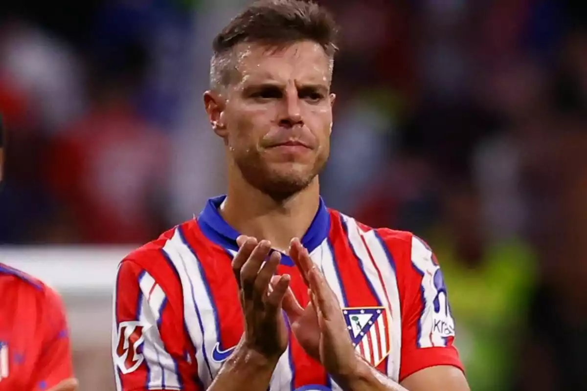 Football player in Atlético de Madrid uniform applauding on the field.