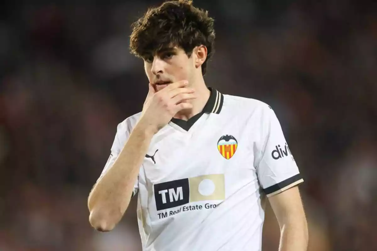 A football player wearing a Valencia CF shirt puts his hand to his face during a match.