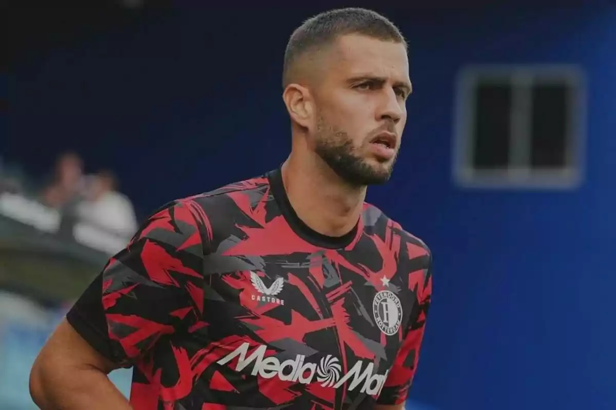 A football player in a red and black training shirt with the "MediaMarkt" and "Castore" logos on the chest.