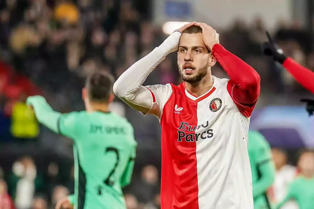 A soccer player in a red and white uniform puts his hands to his head in a gesture of frustration during a match.