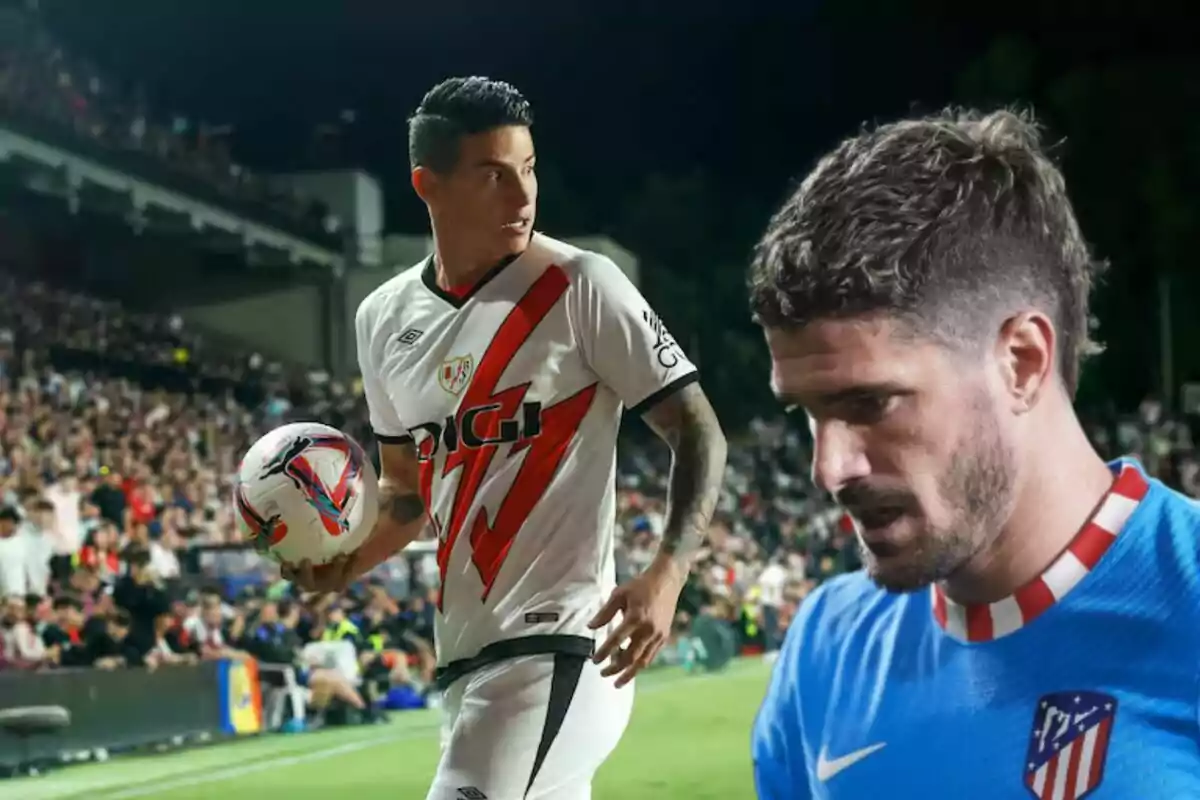 Two soccer players on the field, one in a white and red uniform holding a ball and the other in a blue uniform, with a crowd of spectators in the background.