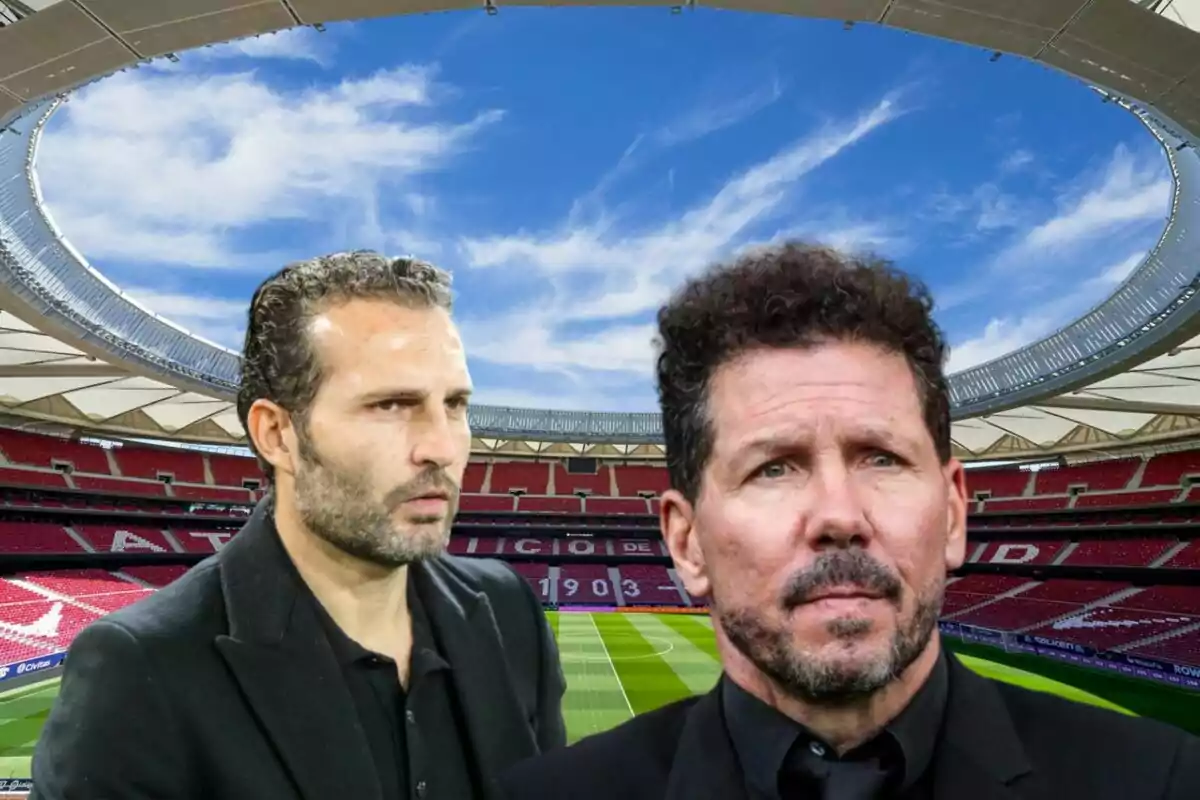 Two men in dark suits in a football stadium with a blue sky in the background.