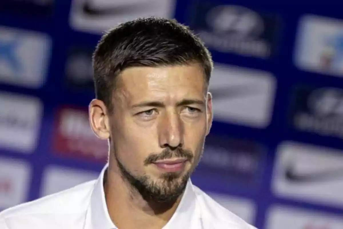 Man with beard and short hair at a press conference with blurred background of logos.