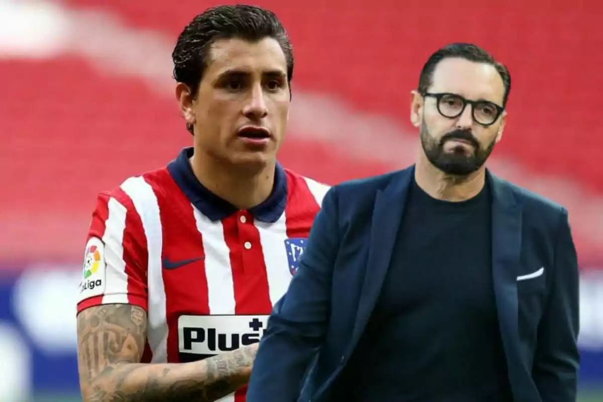 A football player in an Atlético Madrid uniform and a man with glasses and a beard dressed in a dark suit are standing in a stadium with a red background.