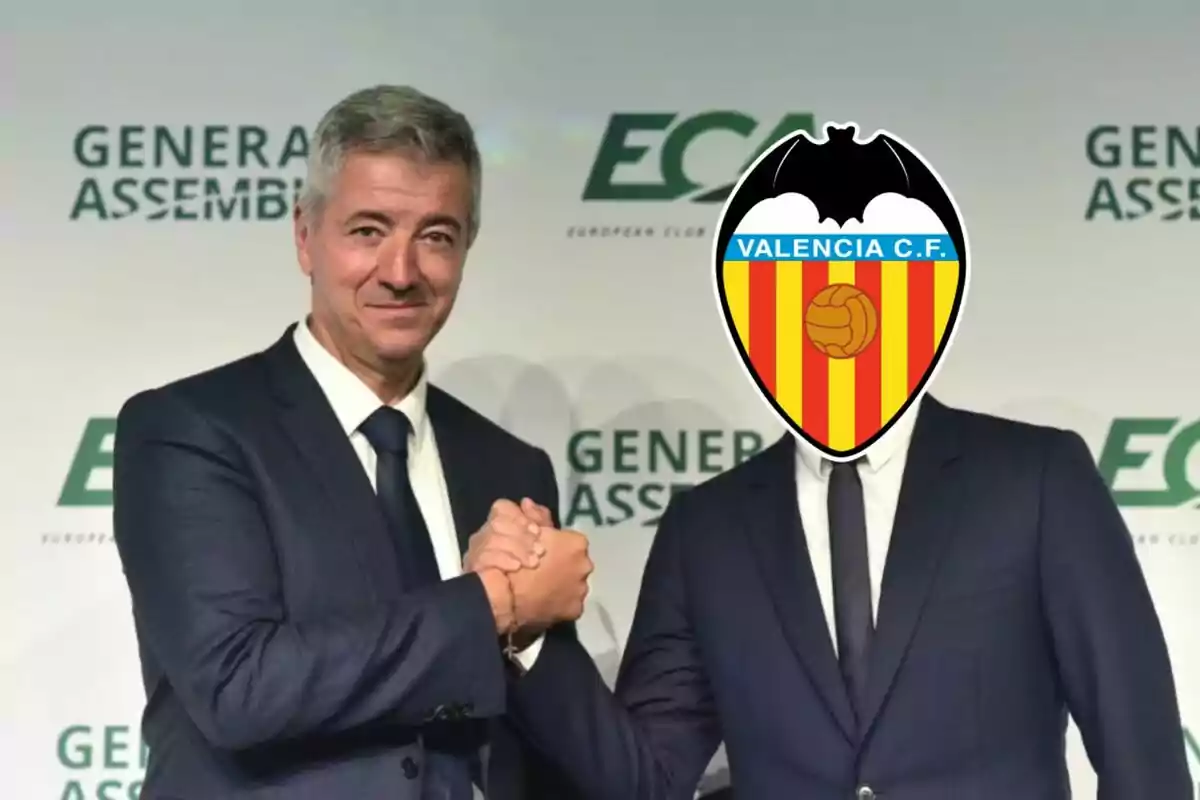 Two men in suits shake hands, one of them has the Valencia C.F. logo on his face.