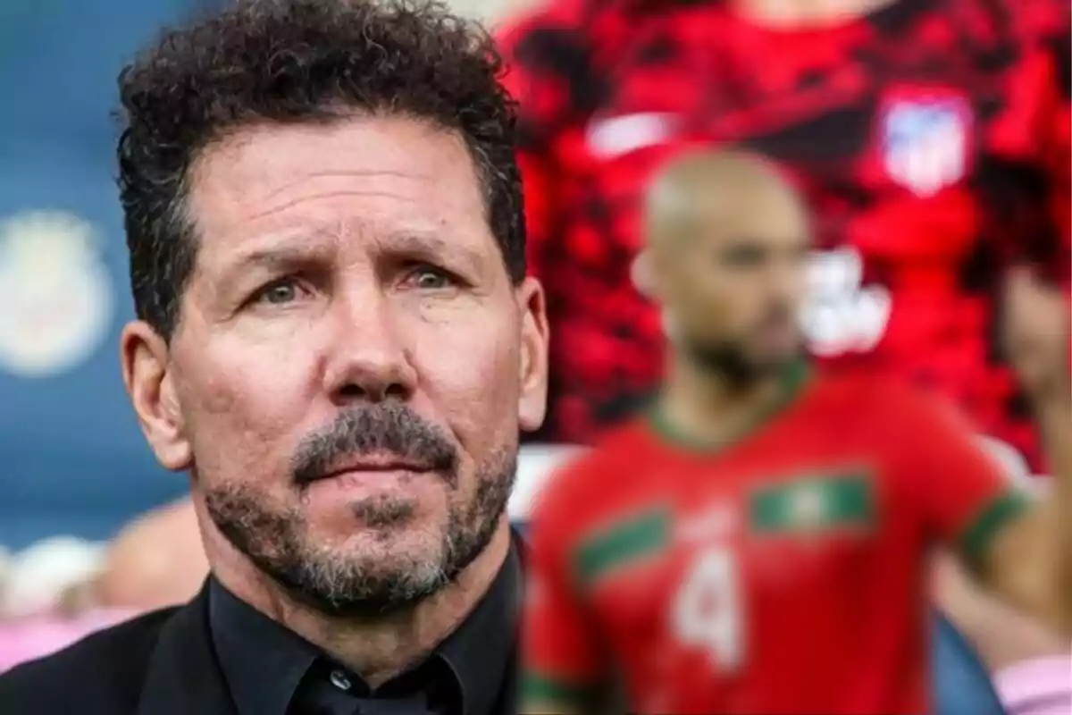 A bearded man with curly hair in the foreground, with a football player out of focus in the background.