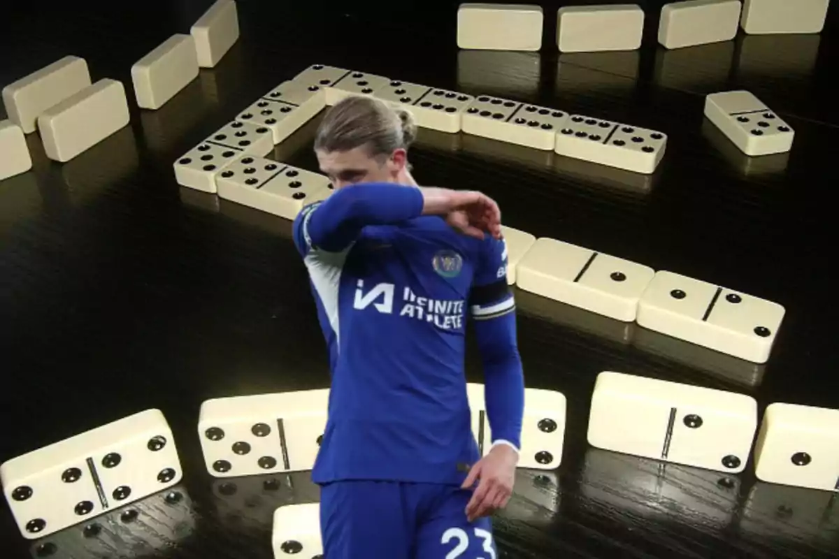 A soccer player in a blue uniform covers his face with his arm while superimposed over an image of dominoes on a black table.