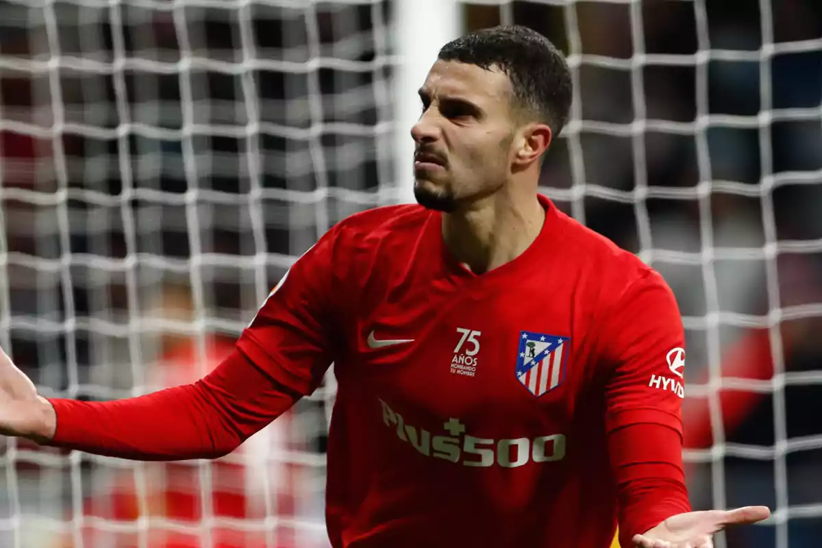 Football player in a red Atlético de Madrid shirt gesturing with outstretched arms in front of a goal.