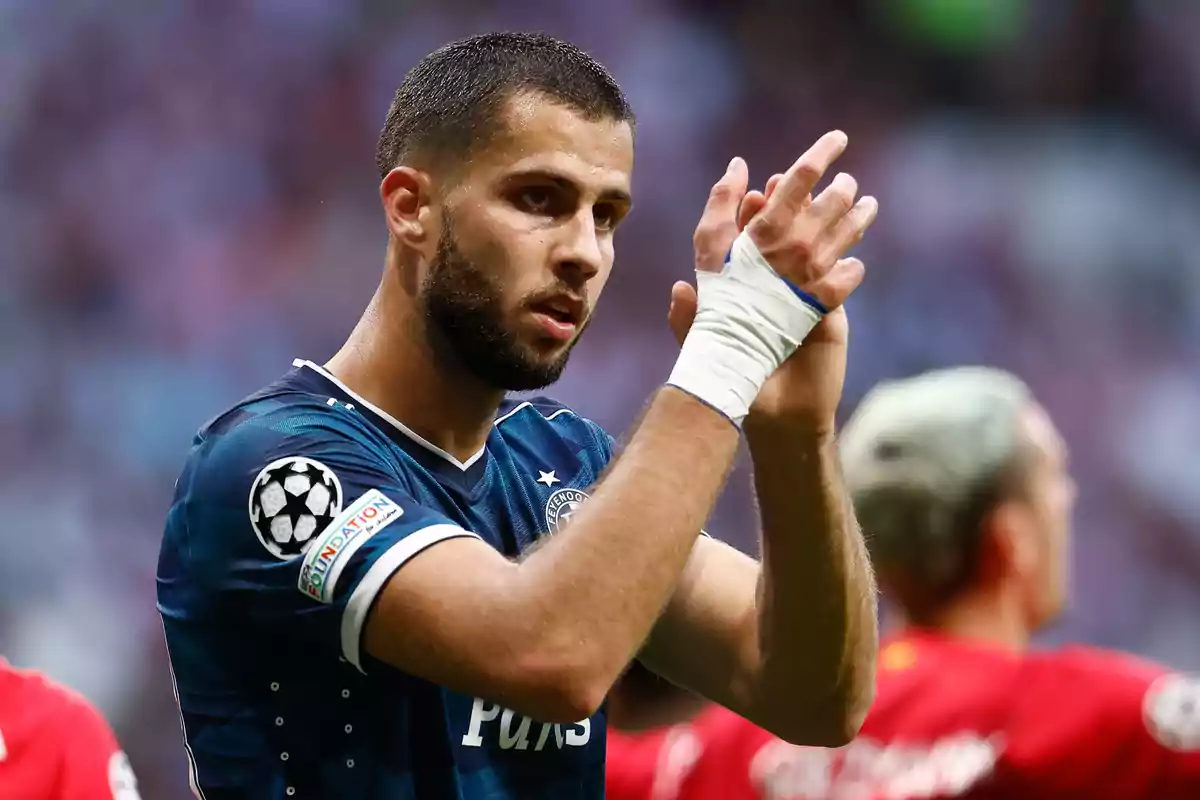 A football player clapping with bandaged hands, wearing a blue uniform with the UEFA Champions League logo on the sleeve.