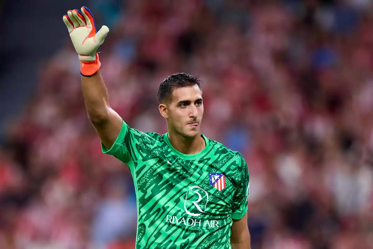 Soccer goalkeeper in green uniform raising his hand in a stadium.