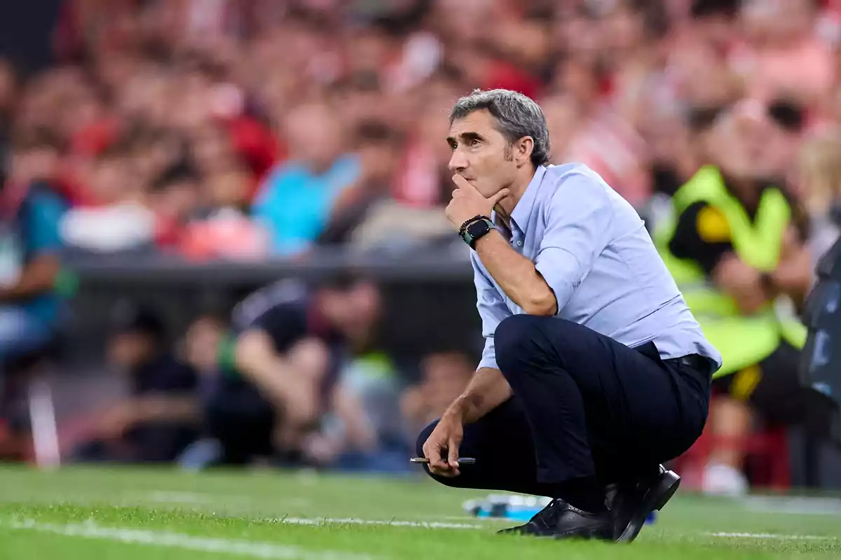 A football coach crouched on the touchline during a match, intently watching the game.