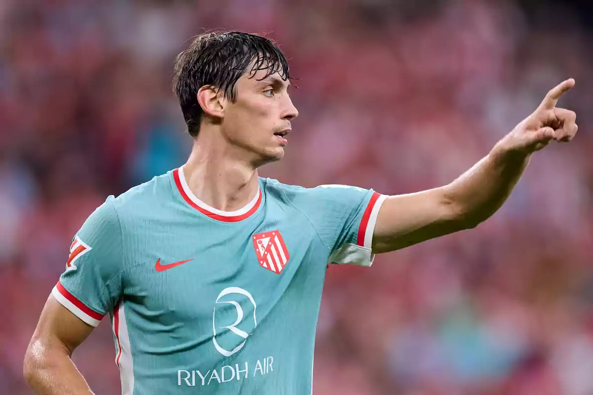 Football player in a light green Atletico Madrid shirt pointing with his finger in a stadium.