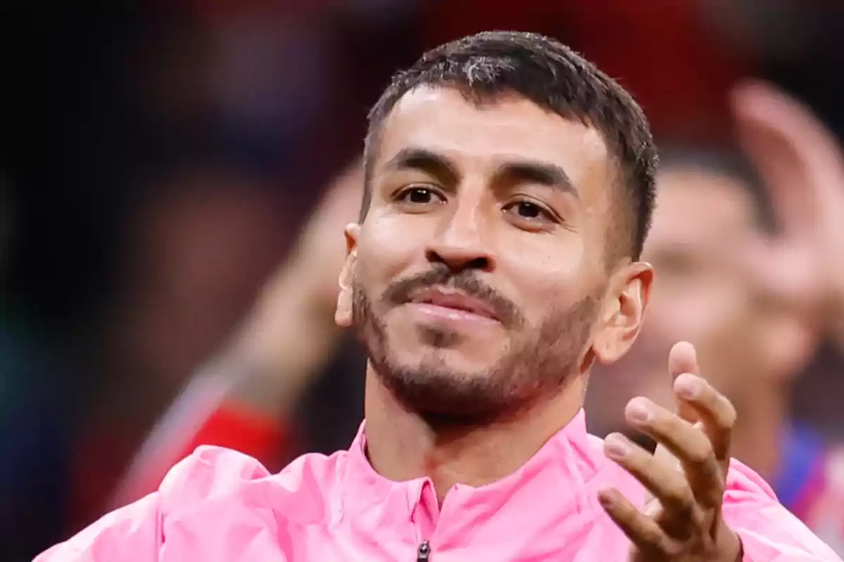 Person in pink jacket smiling and applauding at a sporting event.