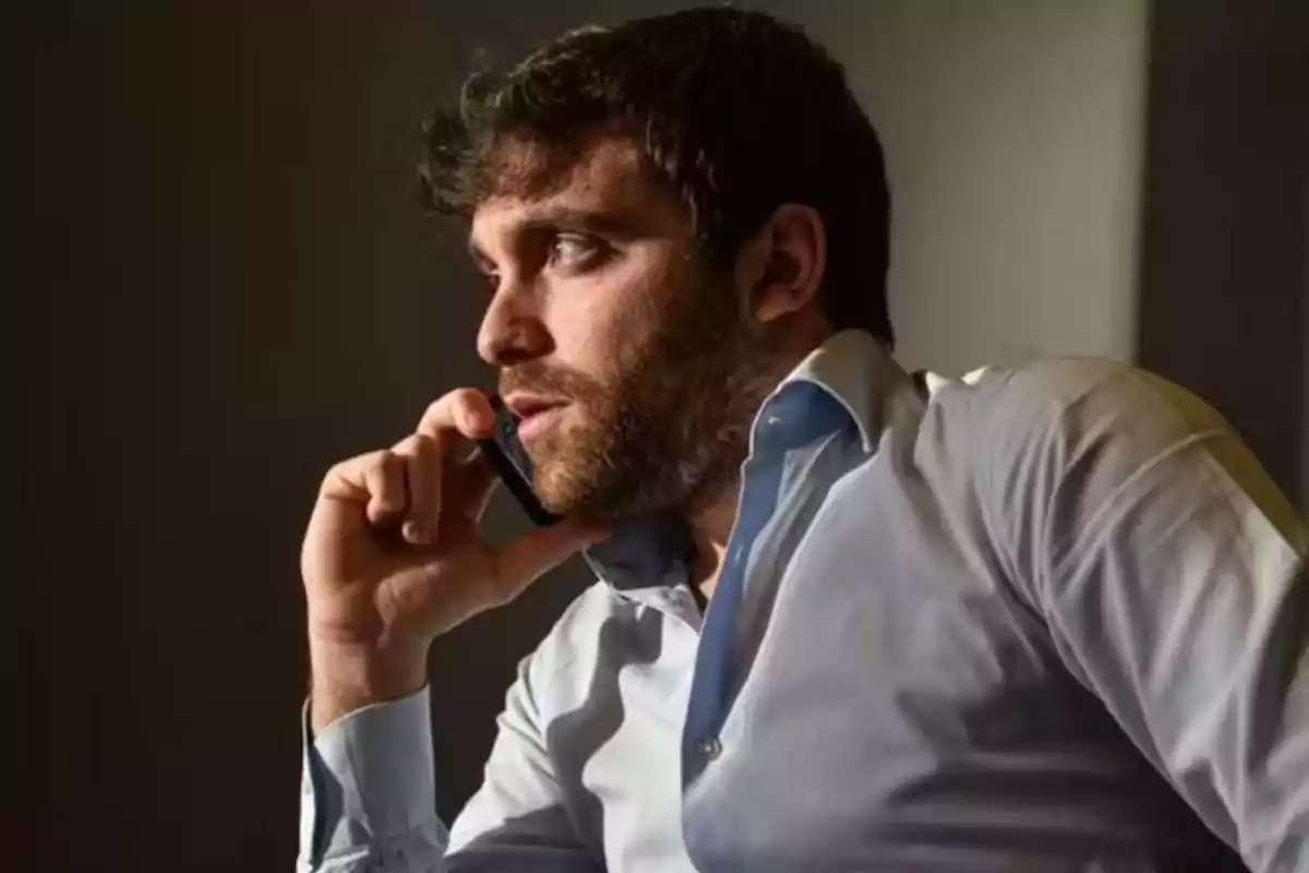 Bearded man talking on mobile phone while wearing a light blue shirt.