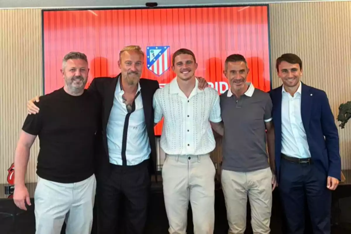 Five men posing together in front of a background with the Atlético de Madrid logo.