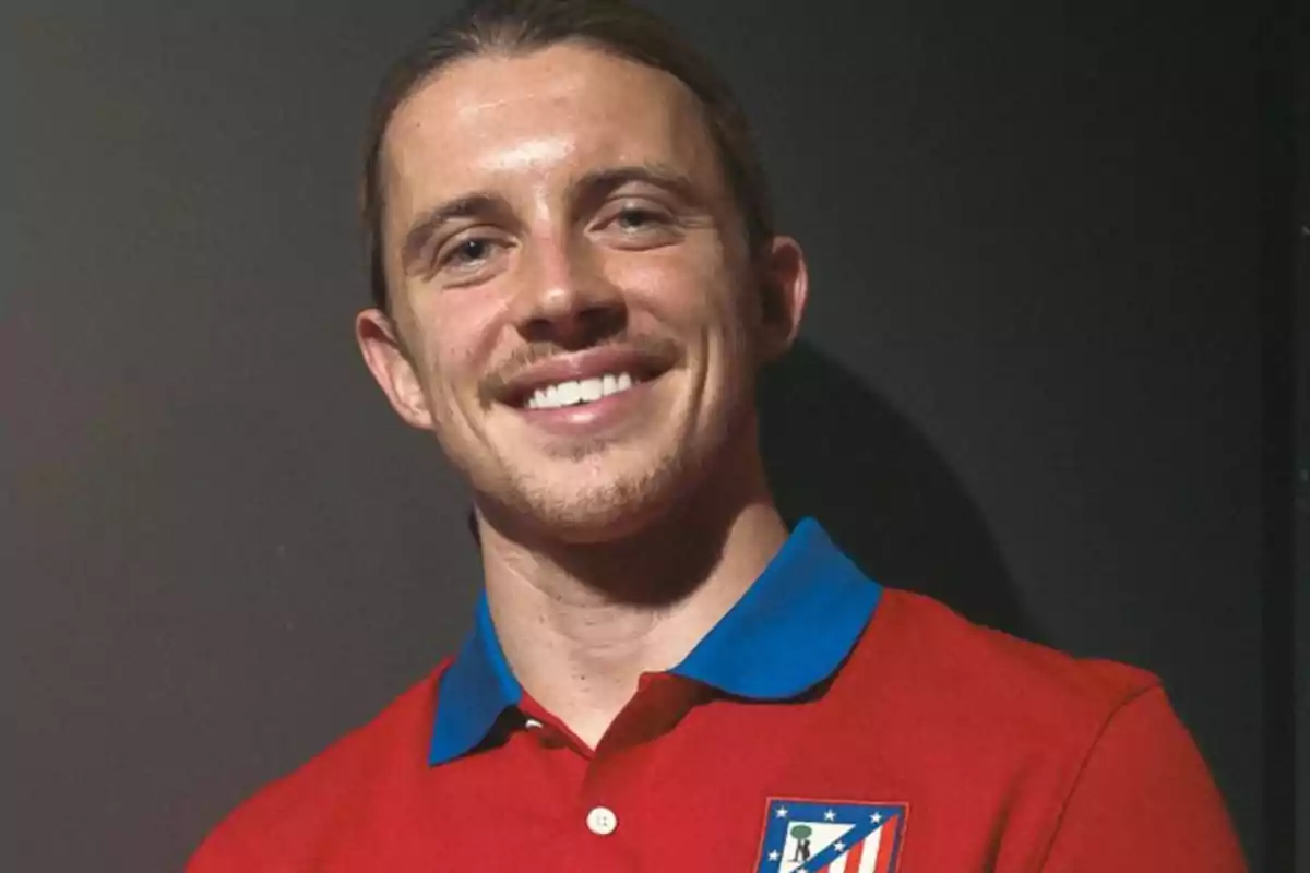 A smiling man in a red Atletico Madrid shirt.