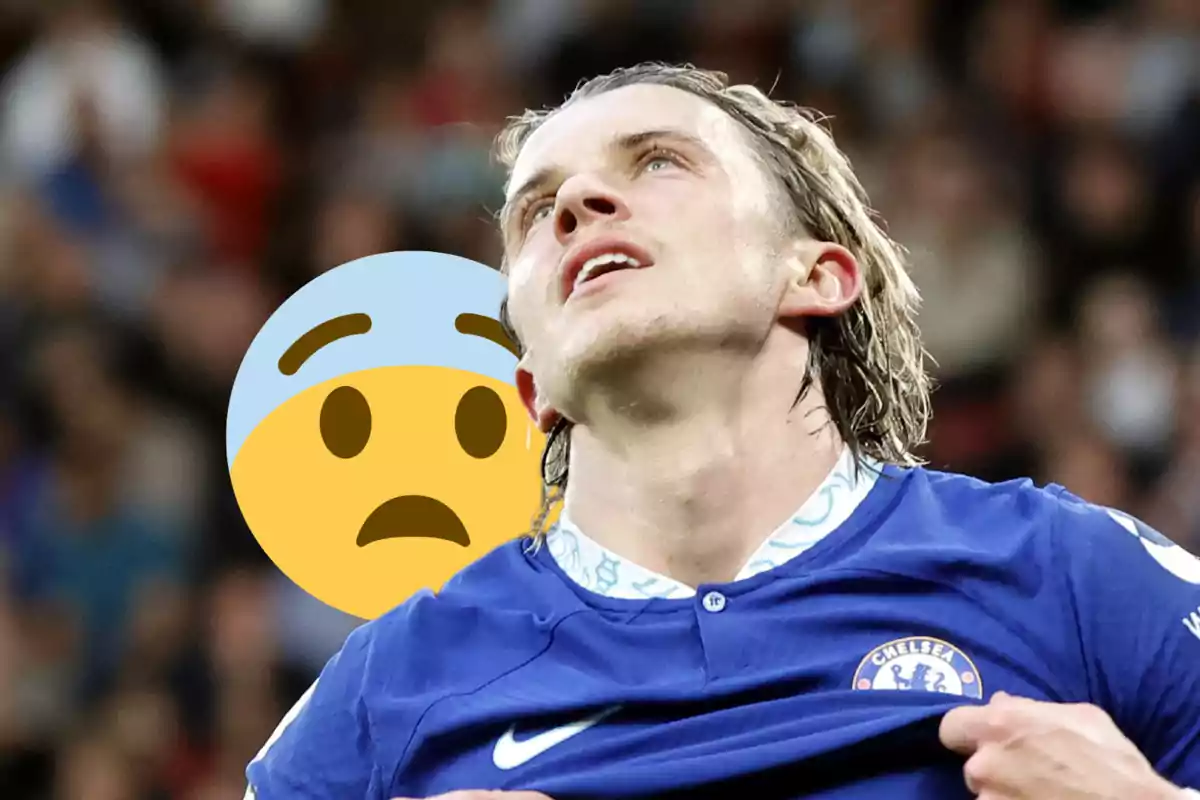 A football player wearing a Chelsea FC shirt raises his head with a frustrated expression as a worried face emoji appears in the background.