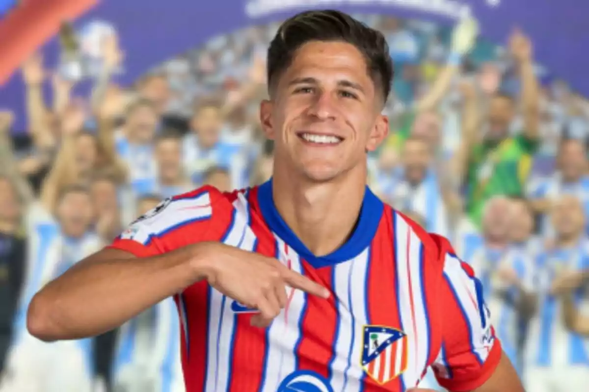 Football player smiling and pointing at the crest on his Atlético de Madrid shirt.