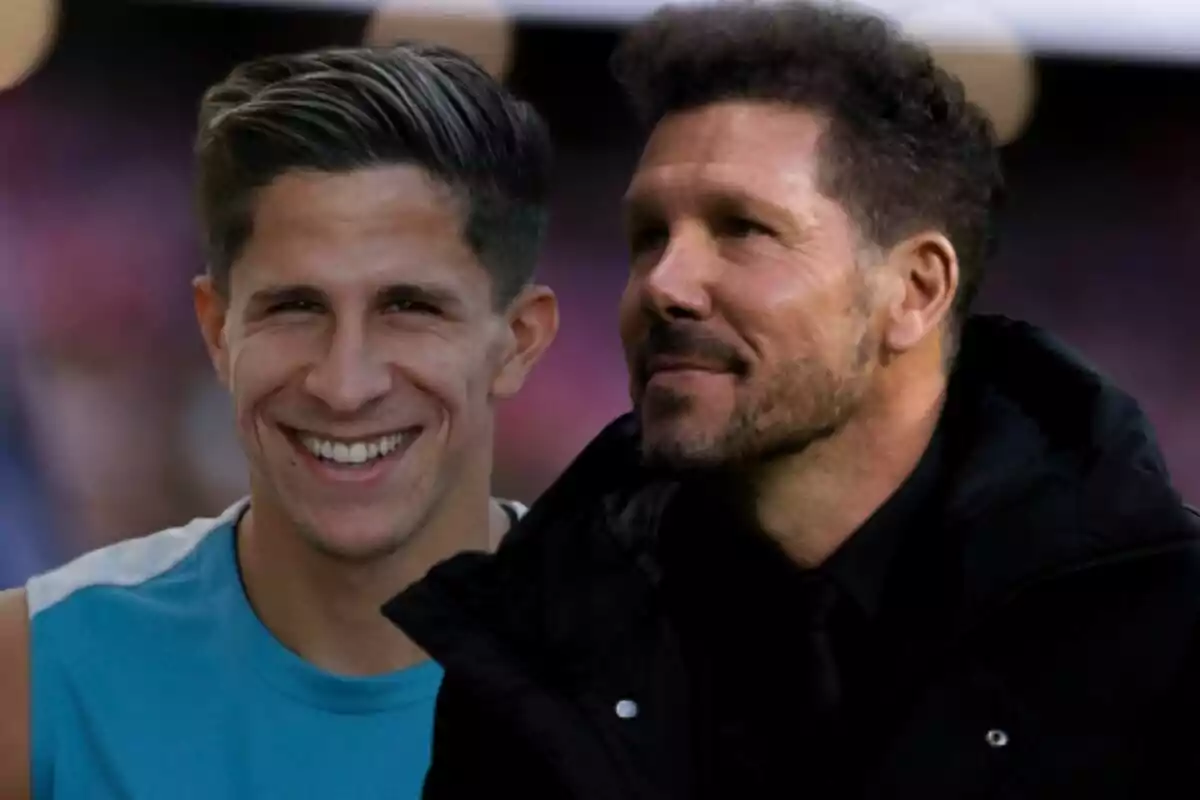 Two smiling men, one in a sports shirt and the other in a black jacket, pose together.