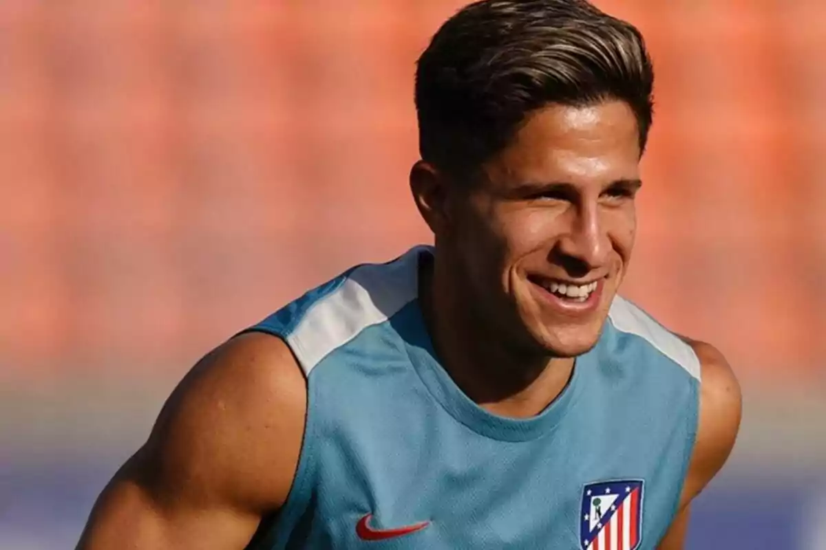 A soccer player smiles as he trains in an Atletico Madrid sleeveless jersey.