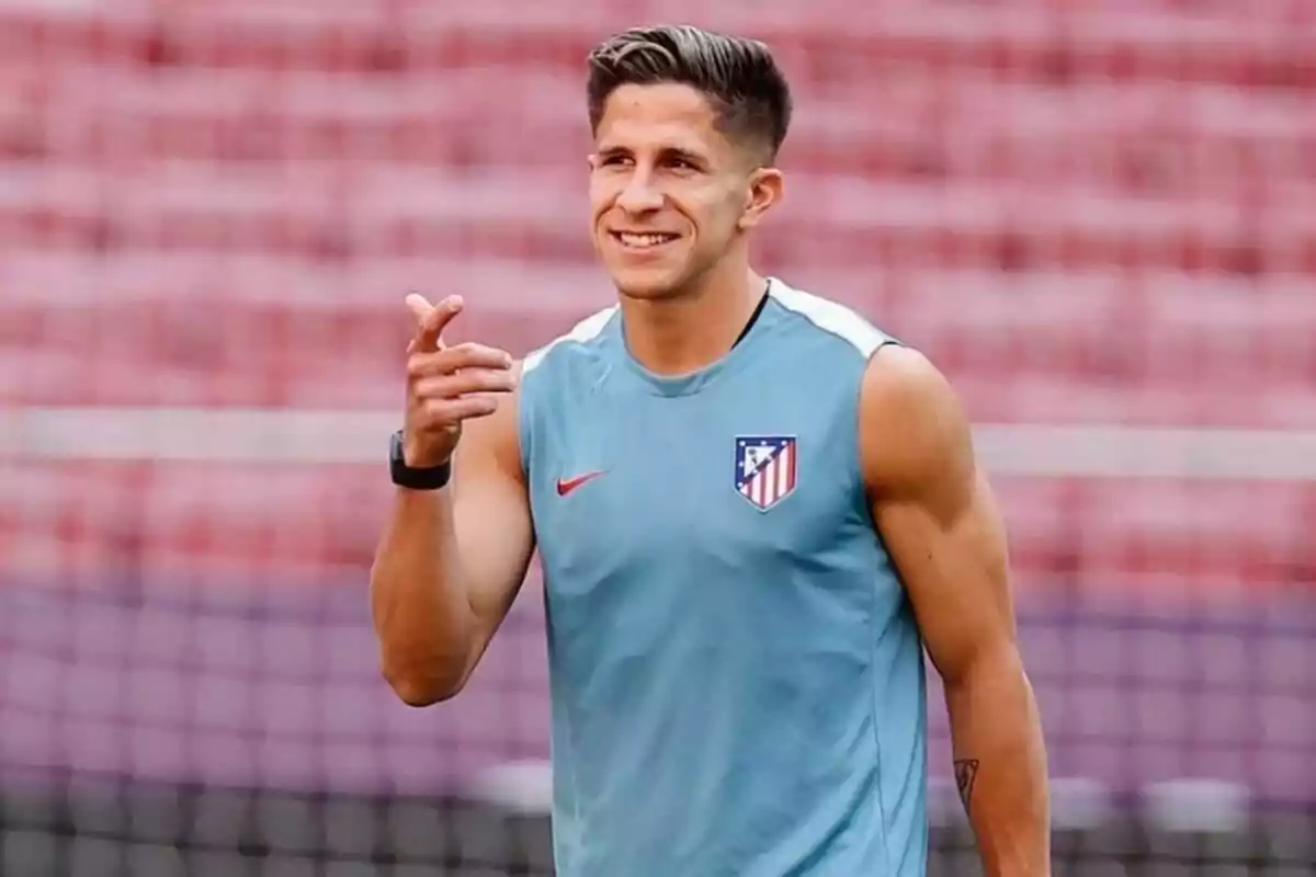 A soccer player wearing an Atletico Madrid training shirt smiles and points with his hand.