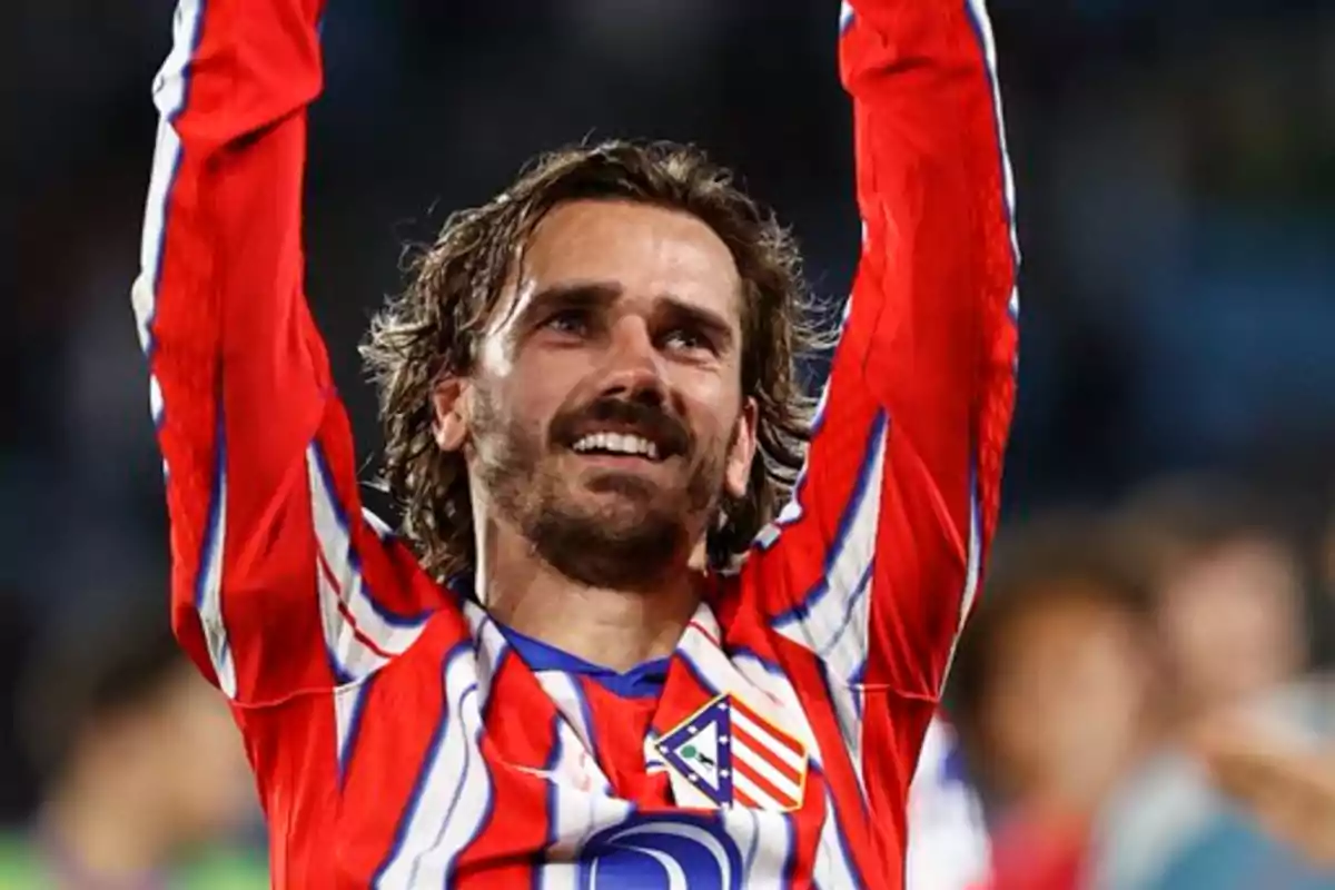 Soccer player in red and white uniform celebrating with arms raised.