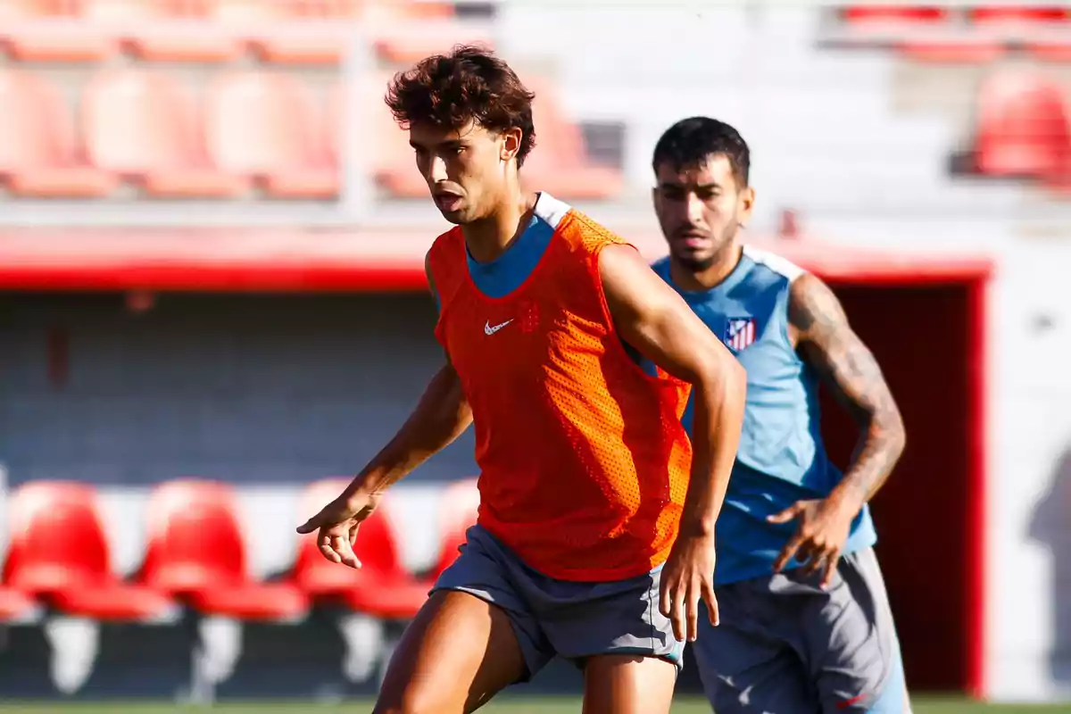 Two soccer players training on a field with red stands in the background.