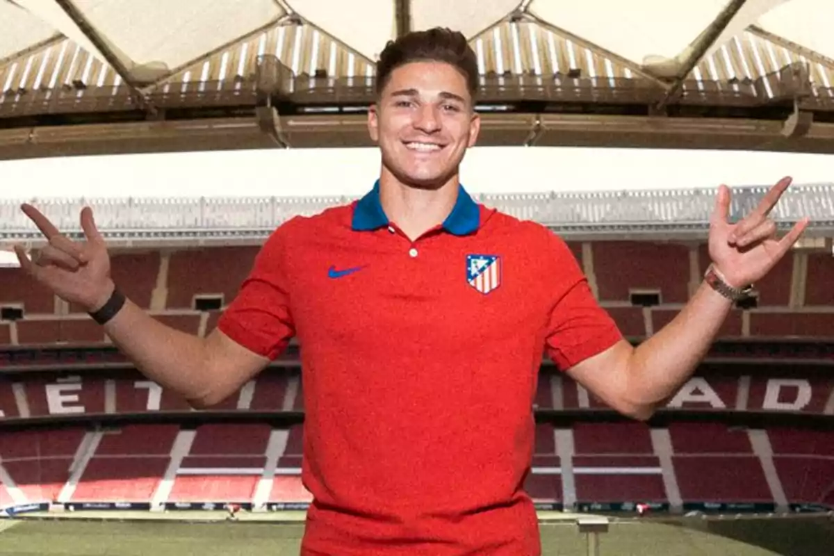 A man in a red Atletico Madrid shirt posing in a football stadium.