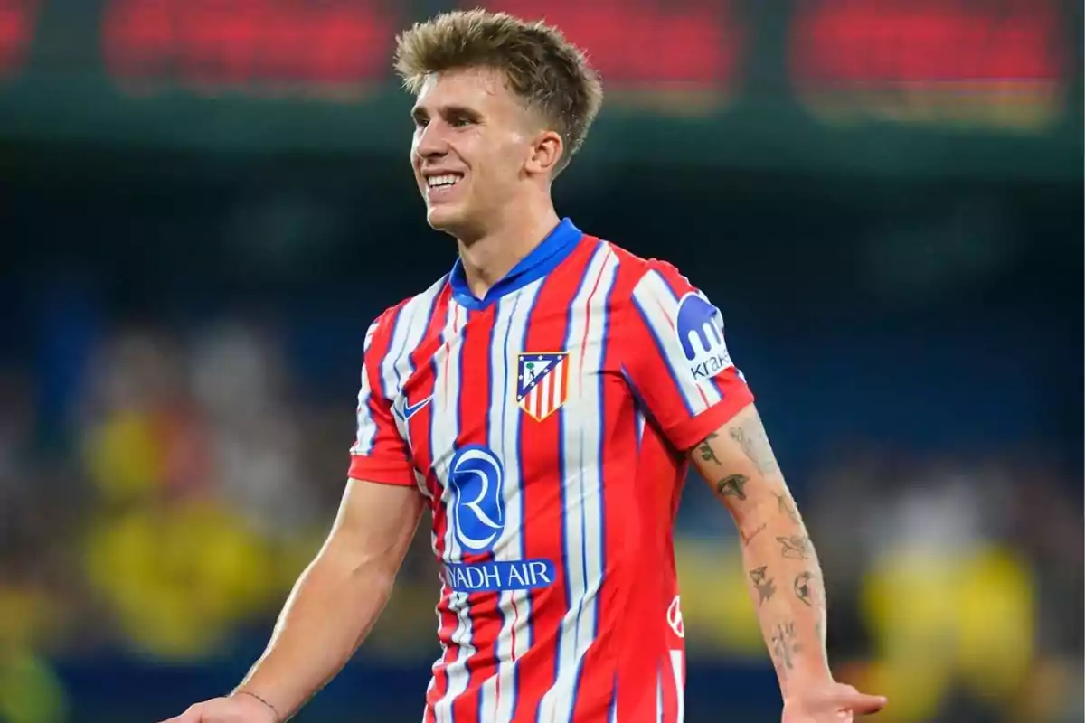 Football player in Atletico Madrid uniform smiling on the field.