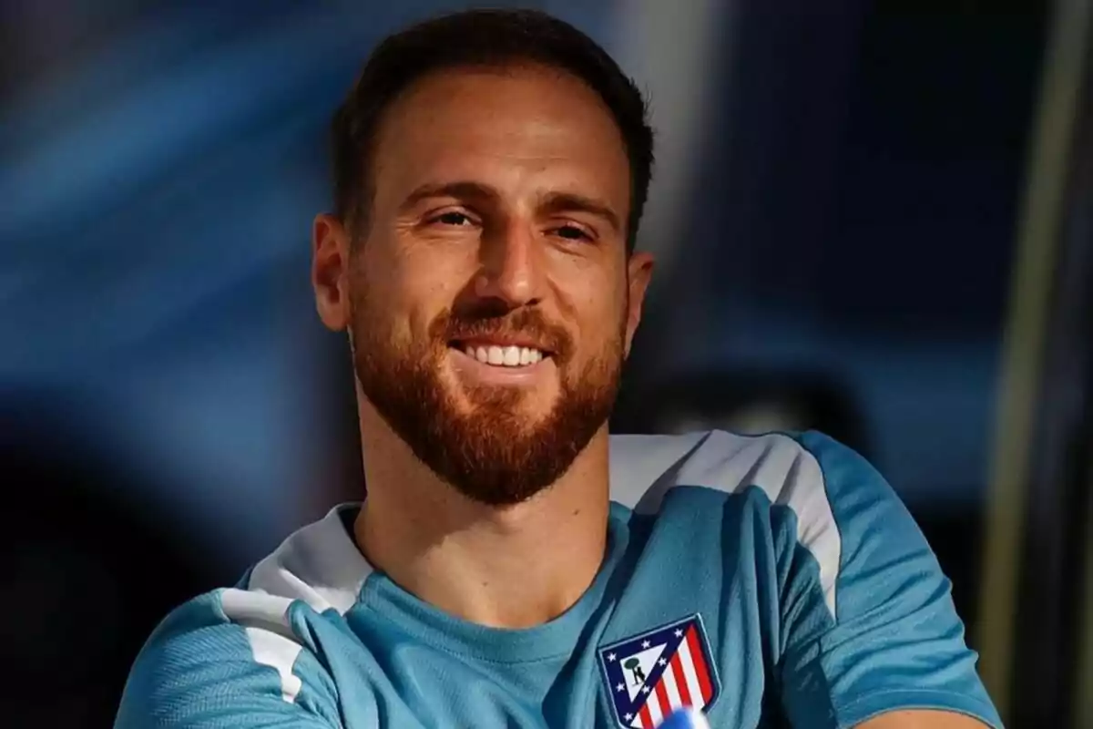 A man with a beard and short hair smiles while wearing a blue sports shirt with the Atlético de Madrid crest.