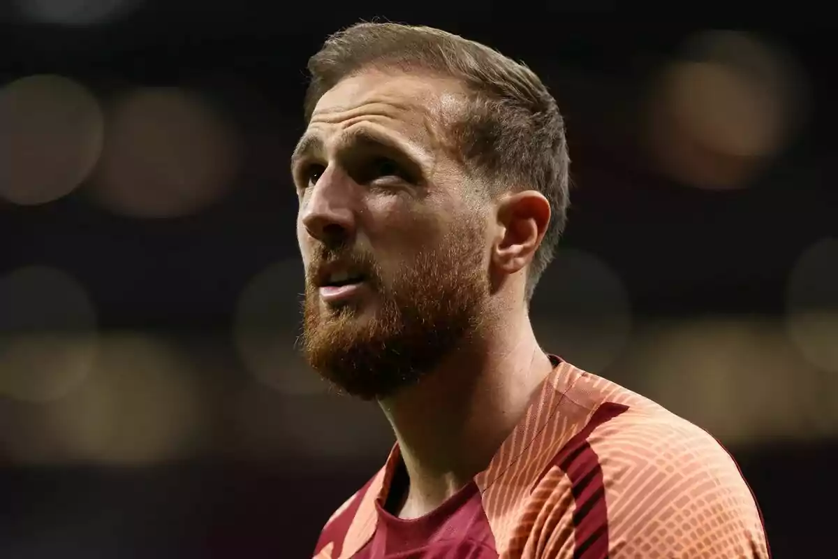 A man with a beard and short hair, wearing a sports shirt, looks up with a serious expression.