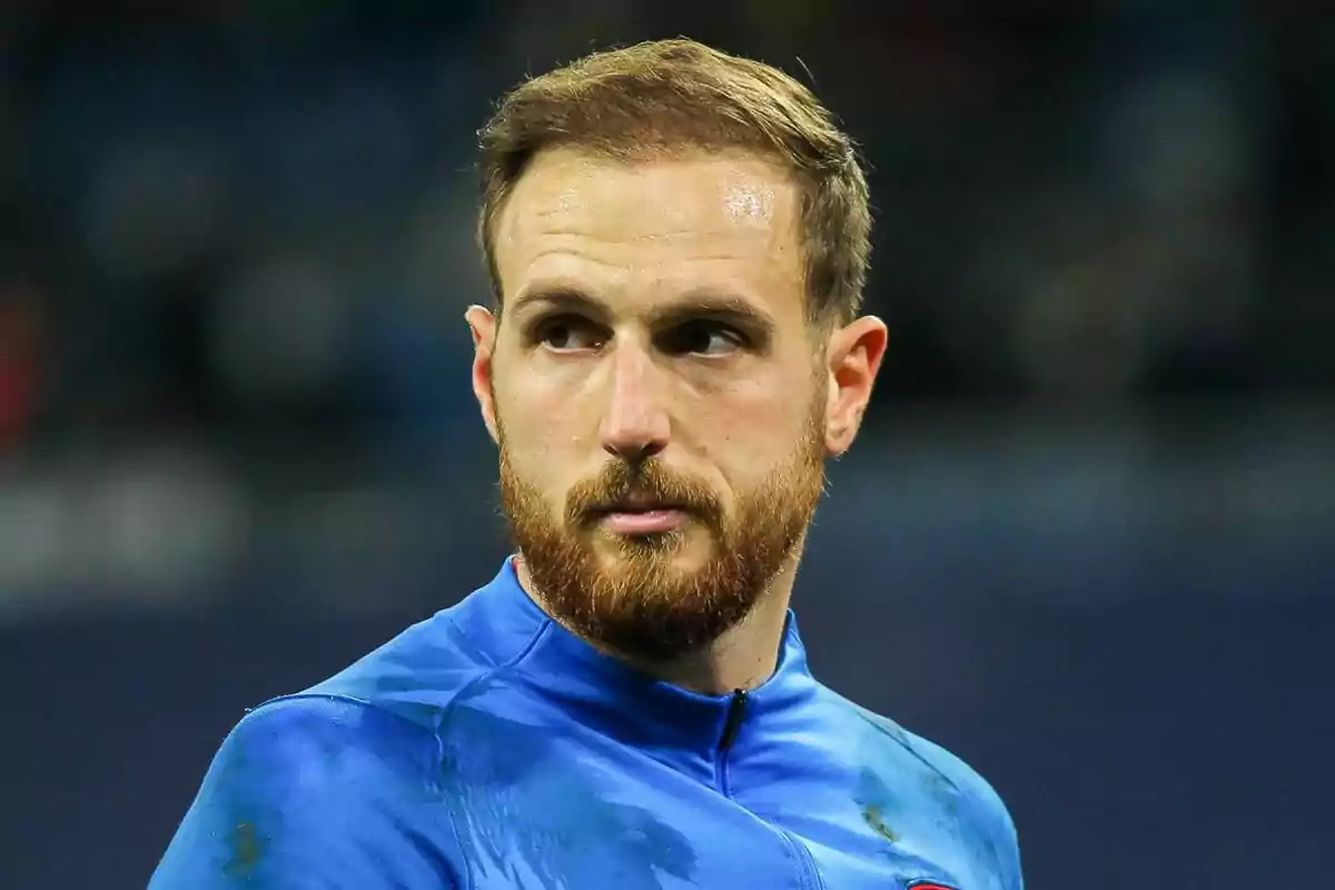 A man with a beard and short hair, wearing a blue t-shirt, looking to the side.