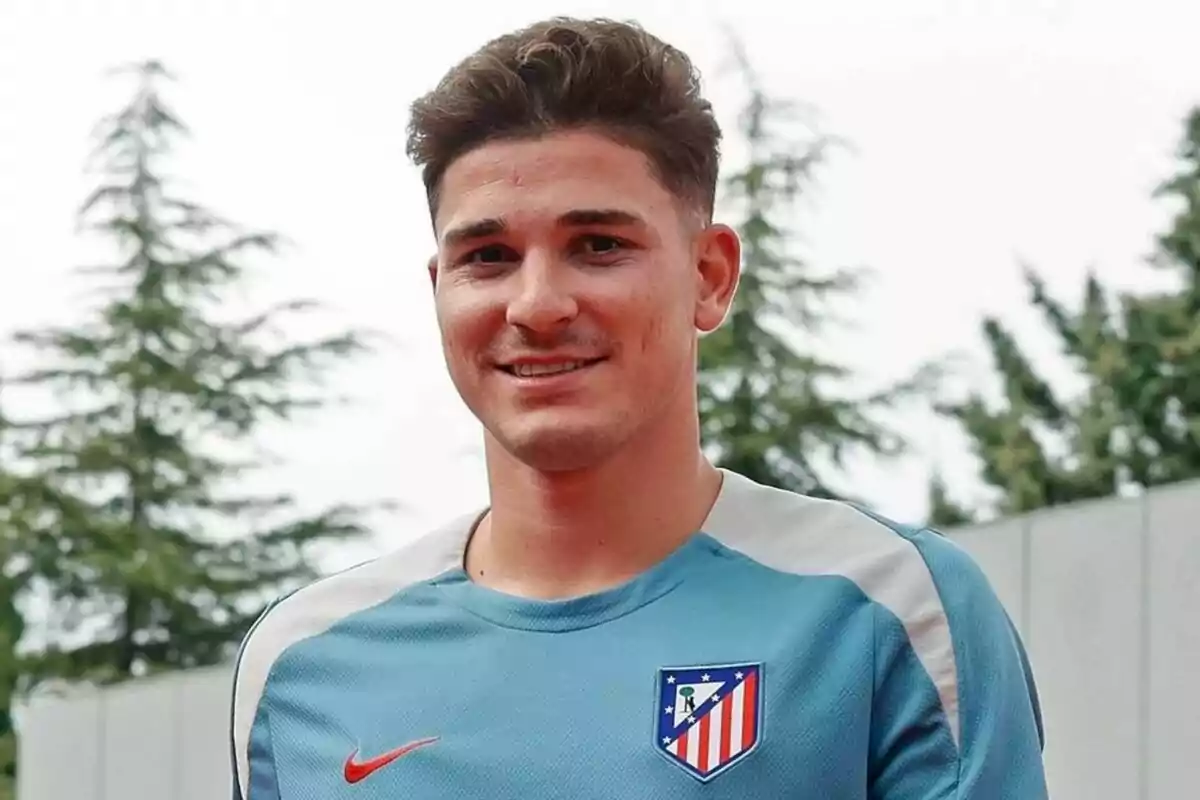 A man in an Atletico Madrid training shirt smiles in front of a backdrop of trees.