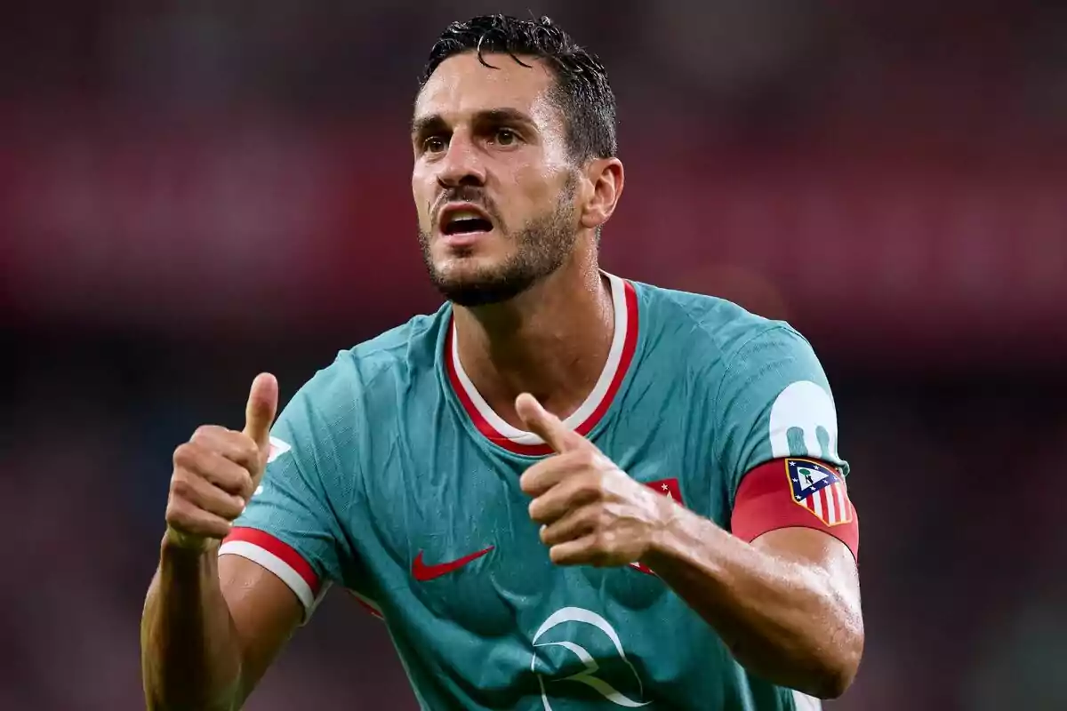 Soccer player in green uniform and captain's armband giving both thumbs up.